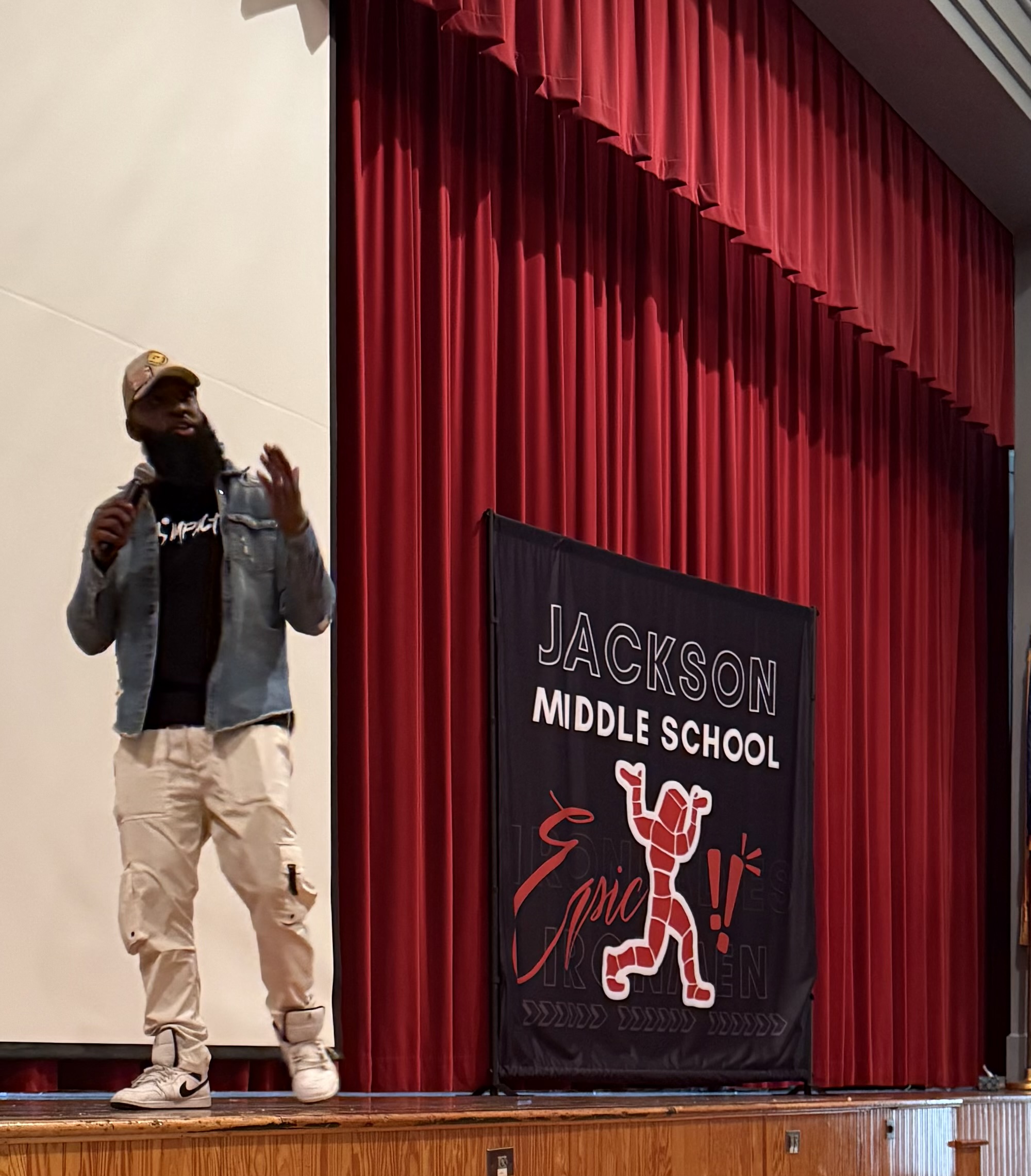 Andre Fluellen speaking with a microphone on stage beside a Jackson Middle School banner