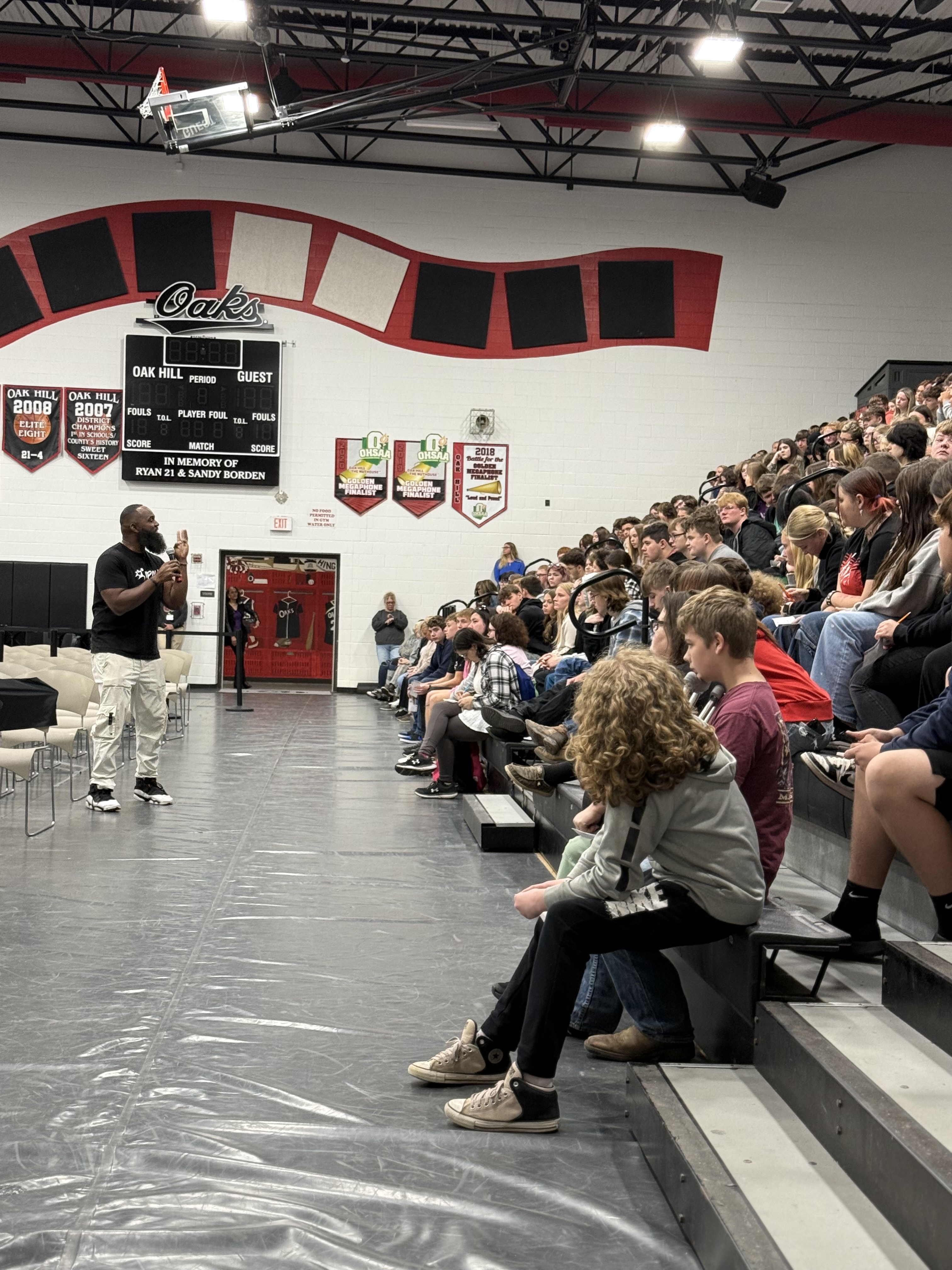 Andre Fluellen speaking to students seated in the bleachers of the Oak Hill school gym