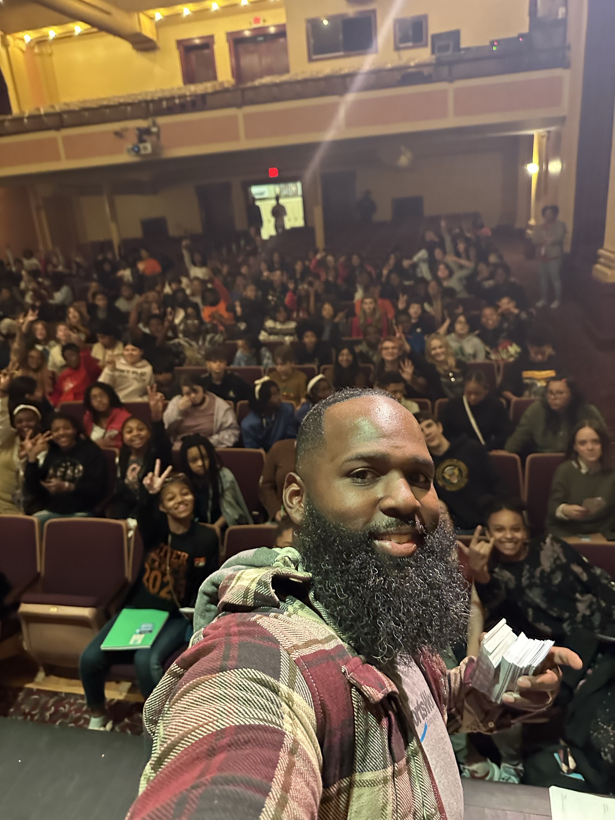 Andre Fluellen taking a selfie from the stage with a full auditorium of smiling students